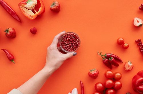 A vibrant display of red fruits and vegetables on a red background with space for text.